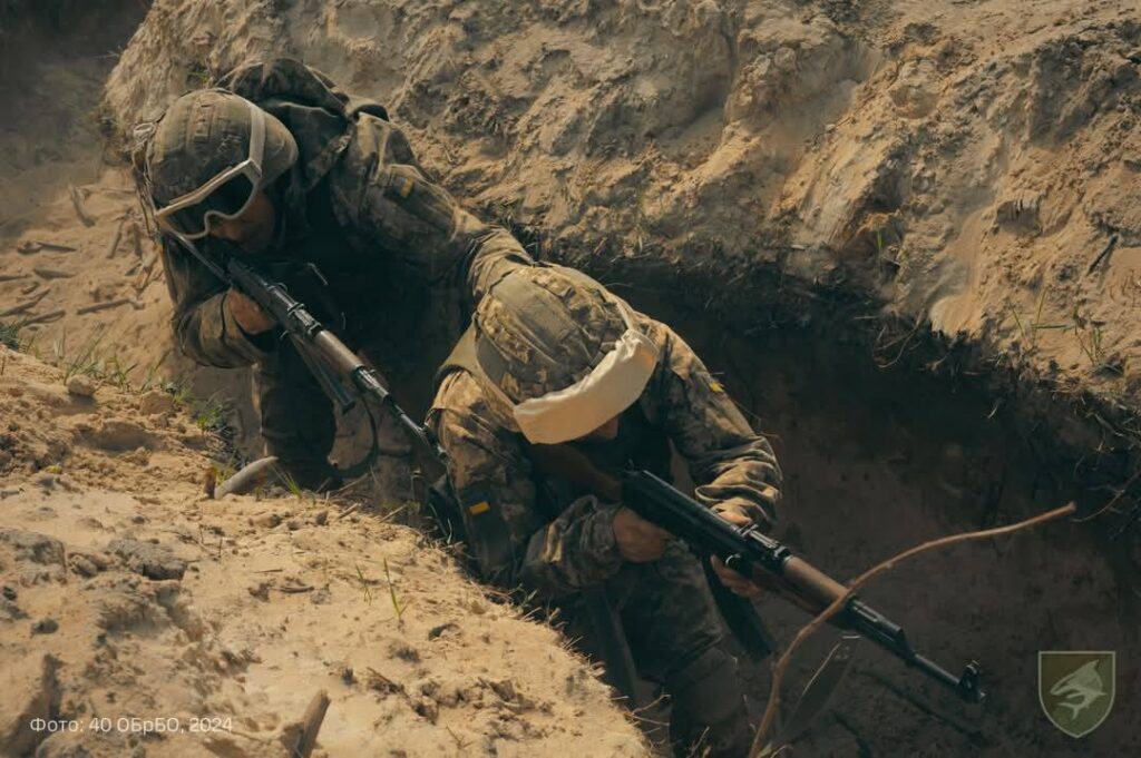 двоє воїнів ідуть, цілячись із зброї, один за одним по окопу