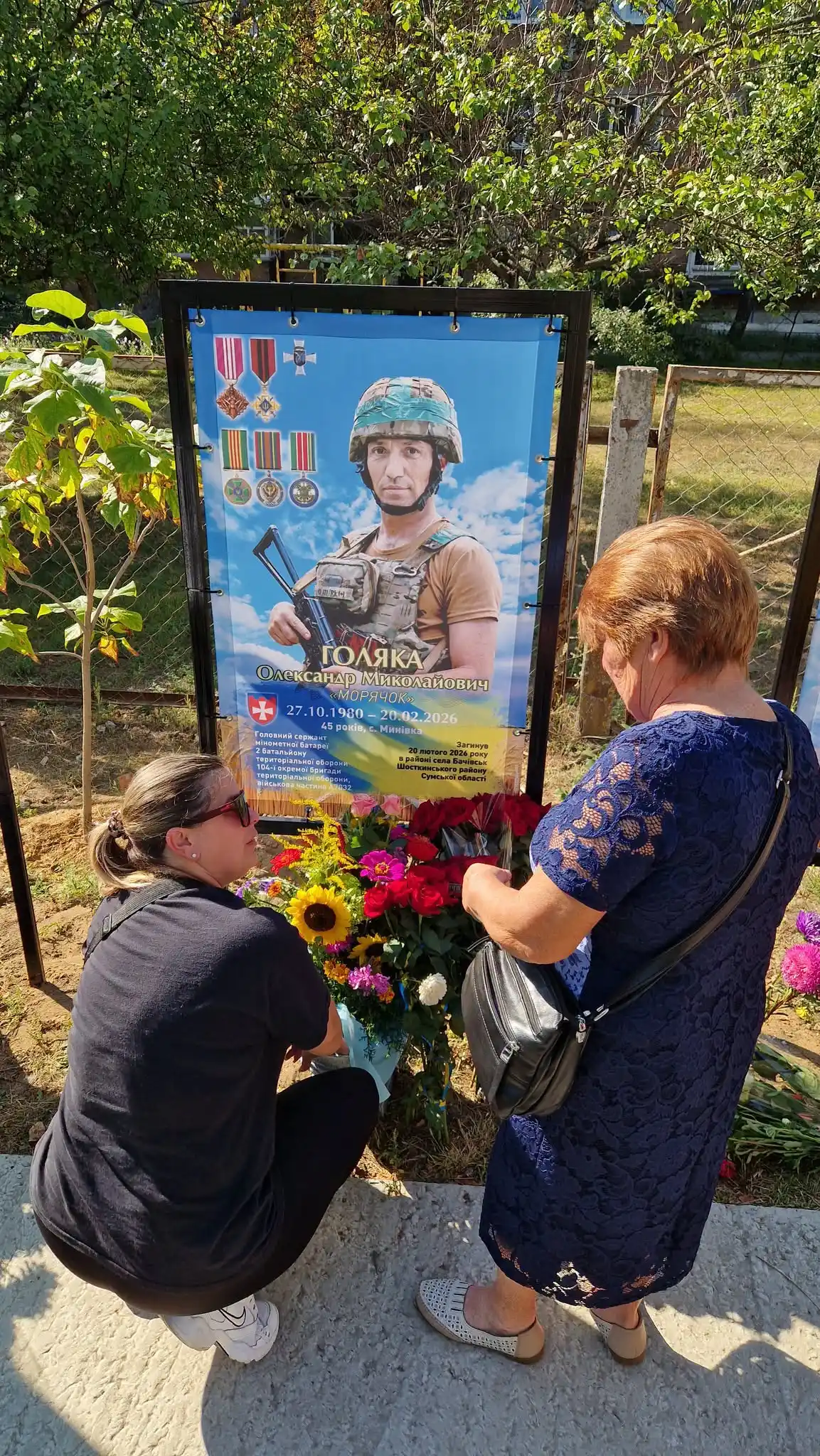 Люди встановлюють квіти біля банера пам'яті