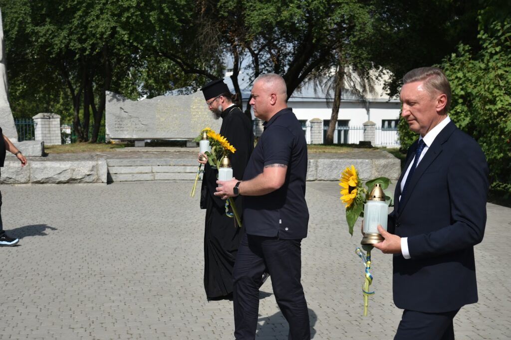 Запрошені гості ставлять лампадки з квітами до меморіалу