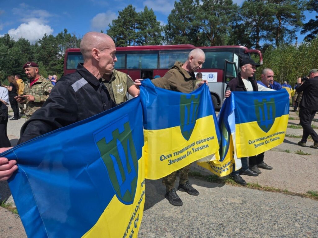 Звільнені з полону військовослужбовці тримають прапори Сил ТрО