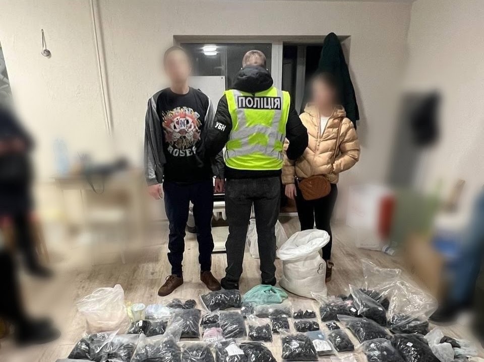 Працівник поліції тримає двох людей, затриманих, на підлозі лежать пакети з наркотичними або психотропними речовинами