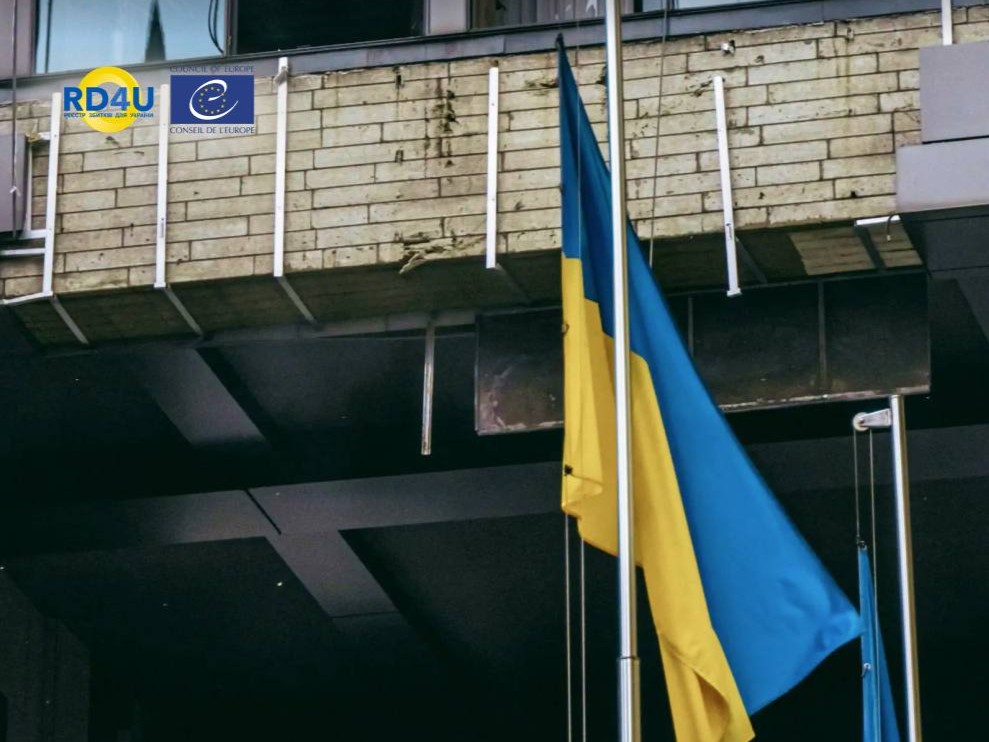прапор України біля пошкодженої будівлі