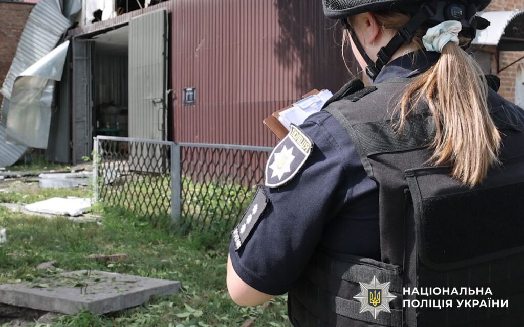 Жінка в поліцейській формі заповнює документи, стоячи біля металевої споруди
