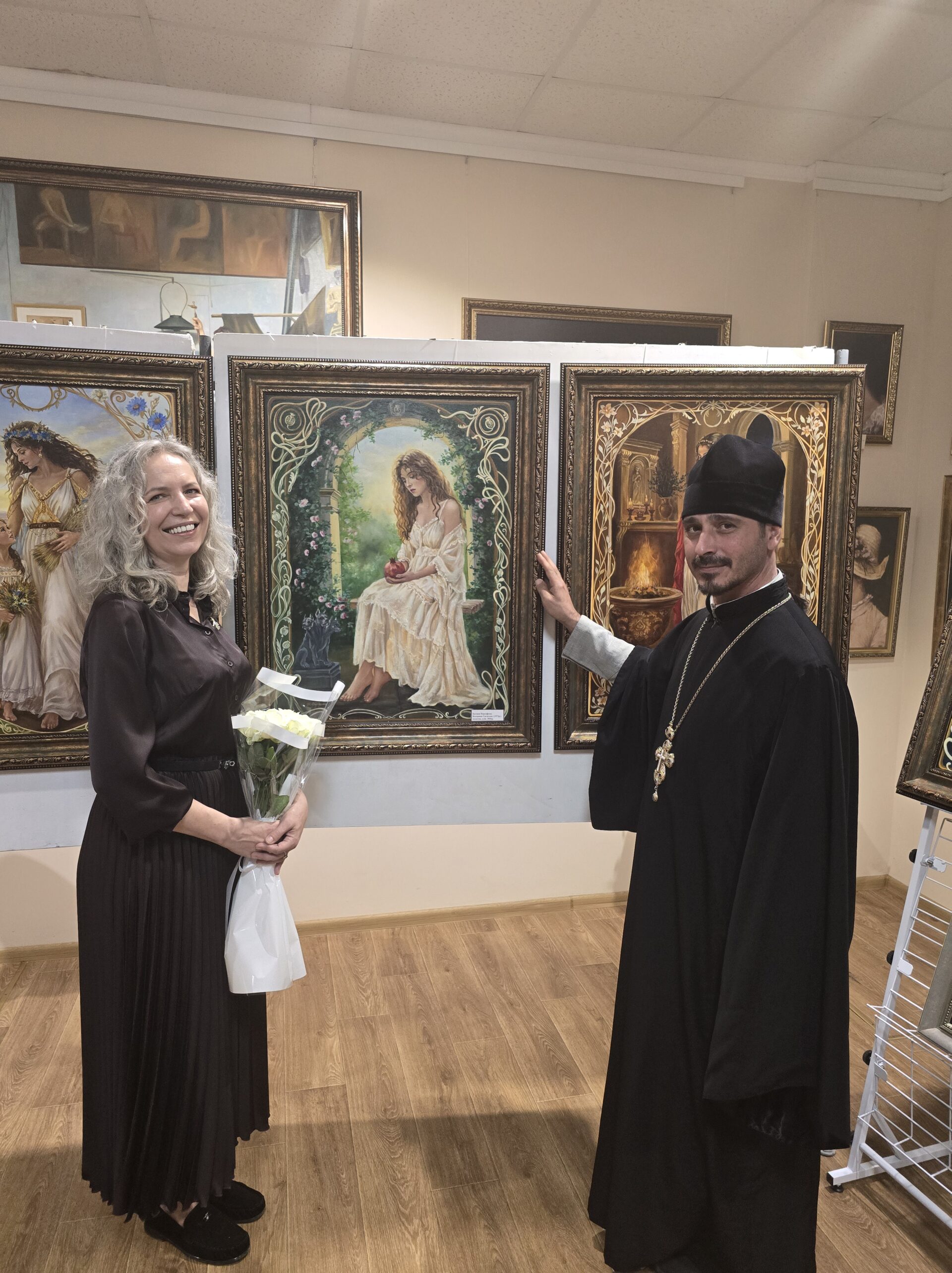 священник і мисткиня з квітами біля картин