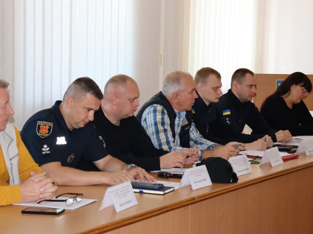 працівники різних установ за столом із табличками з їхніми іменами, прізвищами, посадами