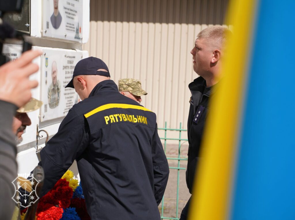 рятувальник кладе квіти до мемоніальної дошки Дмитрові Скрилю