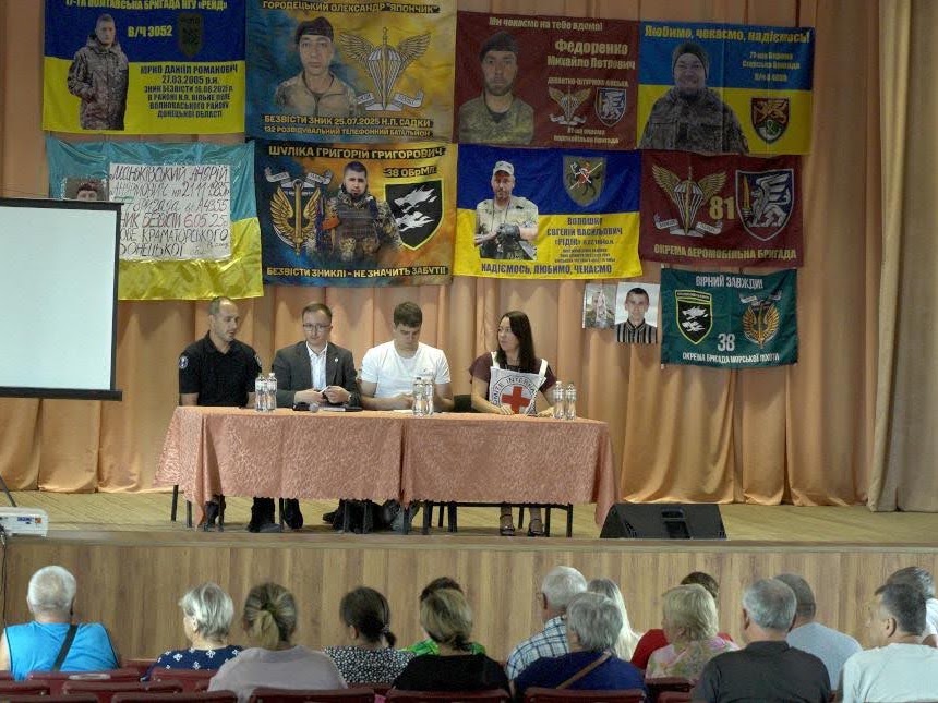чотири людини за столом на сцені та люди в залі
