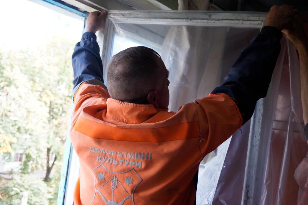 комунальник затягує розбиту шибку плівкою