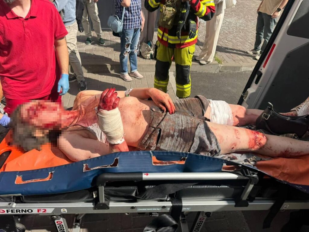 жінку в закривавленому одязі везуть на каталці в машину екстреної медичної допомоги