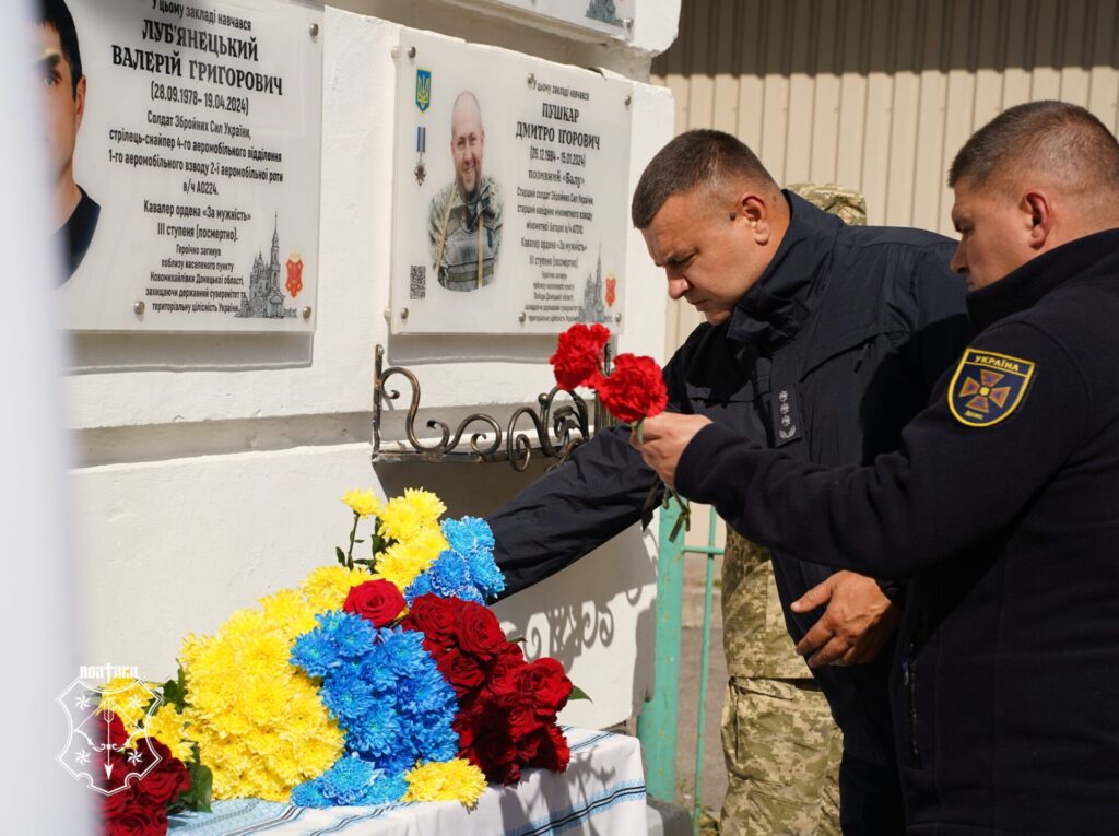 двоє рятувальників кладуть квіти до меморіальної дошки