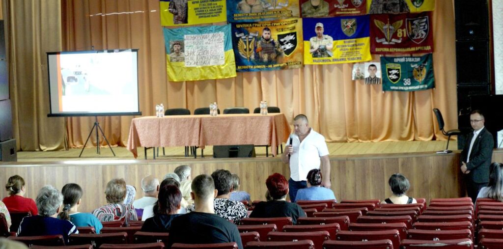 чоловік у білій сорочці спілкується з людьми в залі