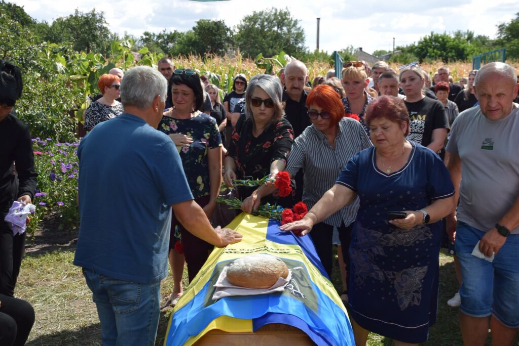 люди кладуть квіти до труни на подвір'ї