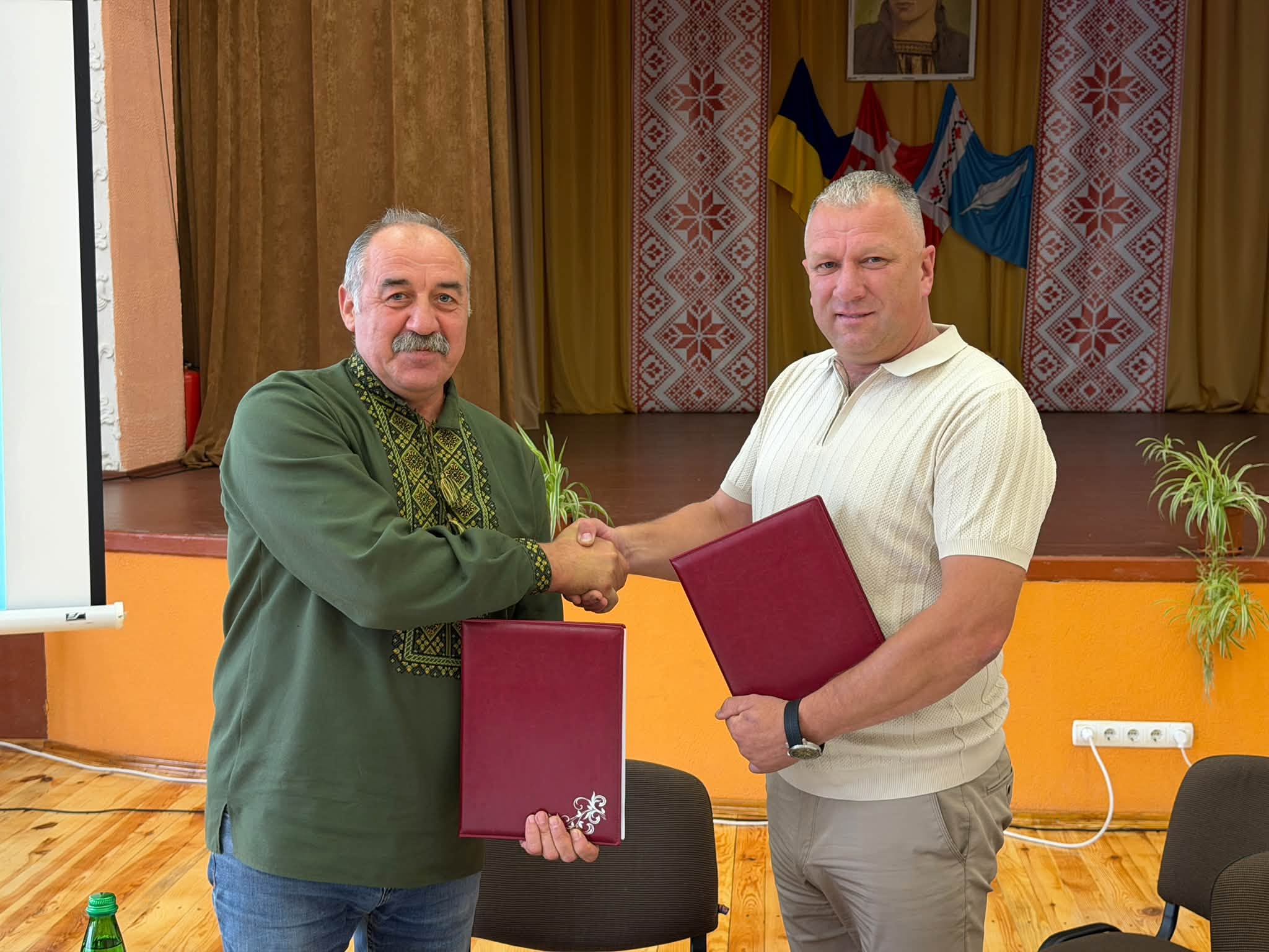 Голови двох громад обмінюються екземплярами меморандуму про співпрацю й тиснуть руку один одному