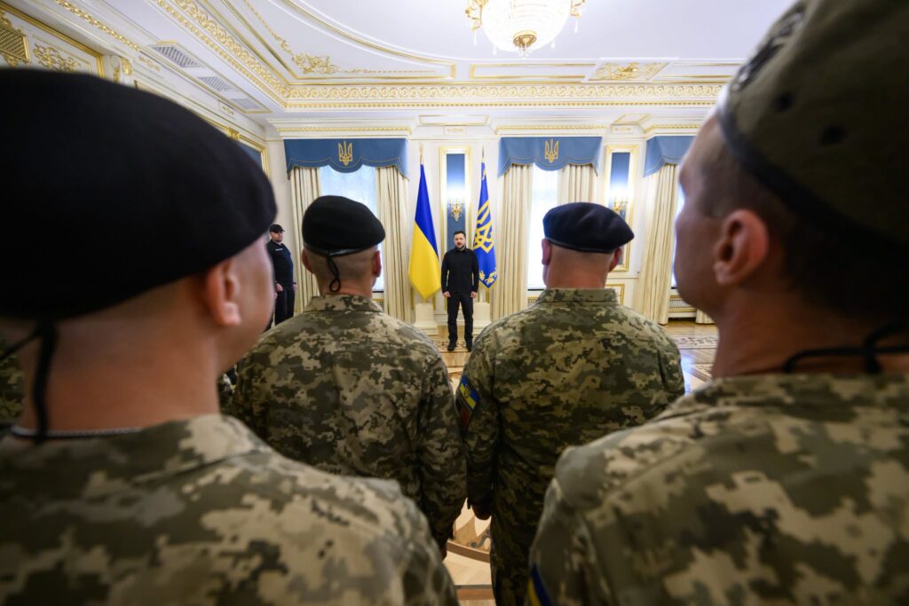 фото з-за спин воїнів, у далечині біля прапорів - президент України