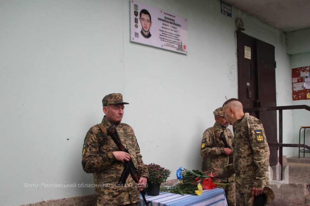 військовослужбовець кладе квіти до меморіальної дошки, у почесній варті поряд стоять двоє військовиків з автоматами
