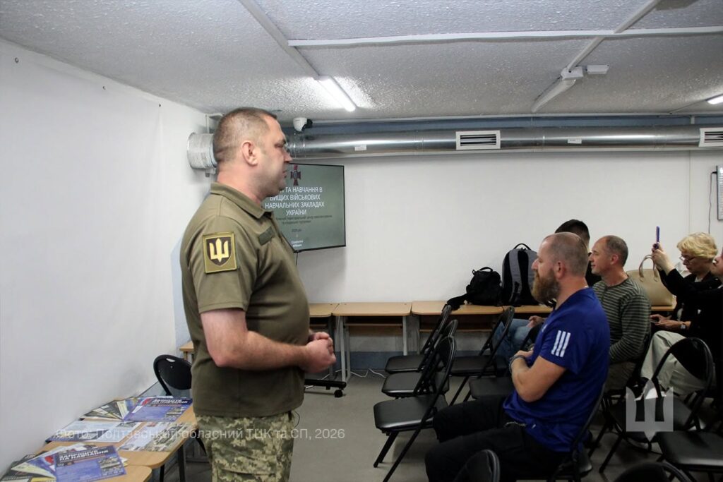 Укриття, військовик виступає перед людьми в залі, поряд із ним екран для демонстрації презентації