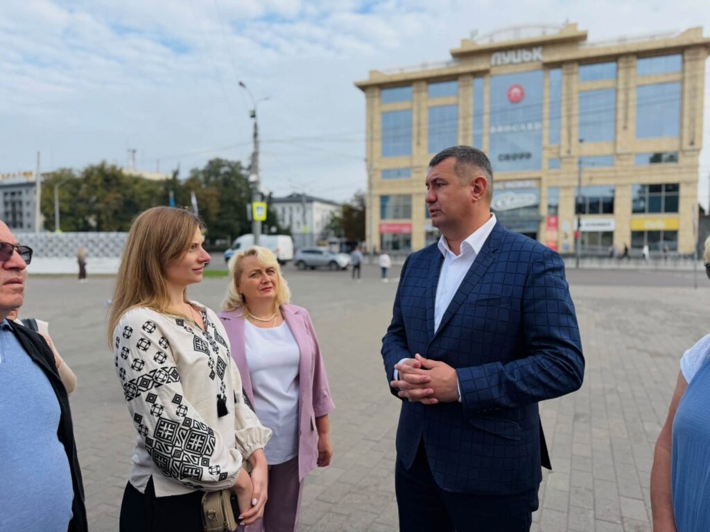 Люди спілкуються на вулиці, позаду будівля з написом Луцьк