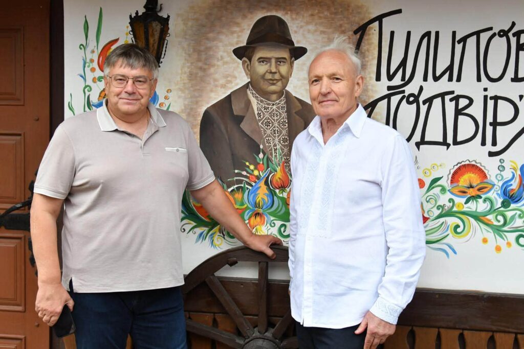 двоє чоловіків на тлі стіни з написом Пилипове подвір'я
