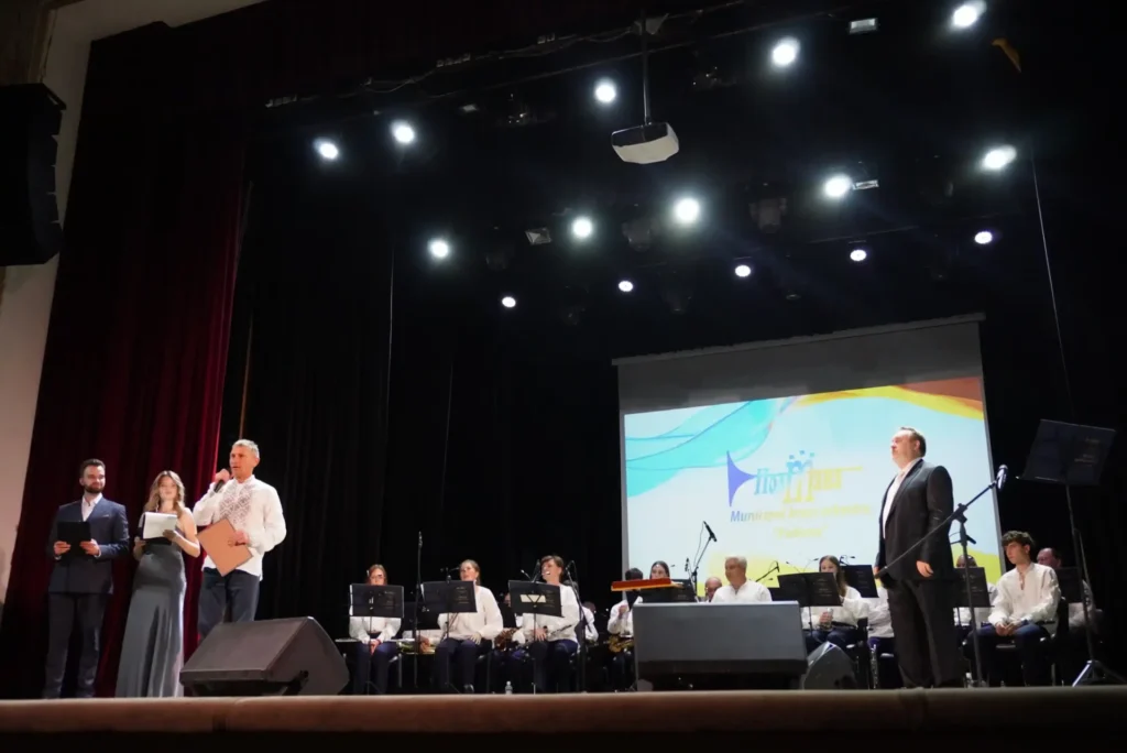 На сцені ведучі, Валерій Пархоменко, оркестр із диригентом, позаду них екран із назвою колективу