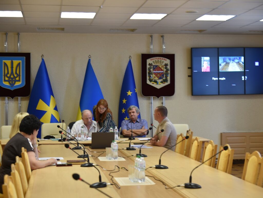 члени комісії та доповідачі сидять за столом у залі засідань