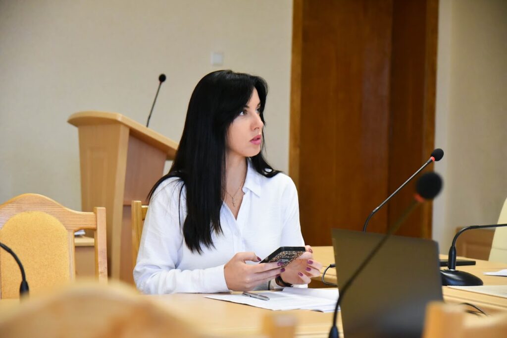 жінка за столом, тримає в руках телефон