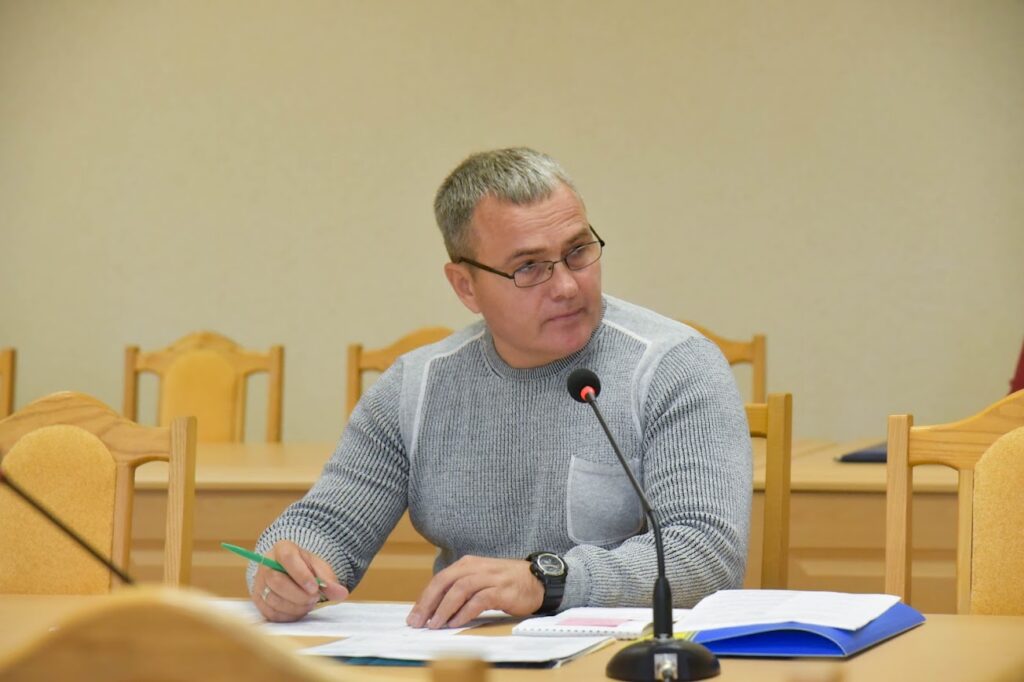 чоловік із документами за столом, перед ним мікрофон