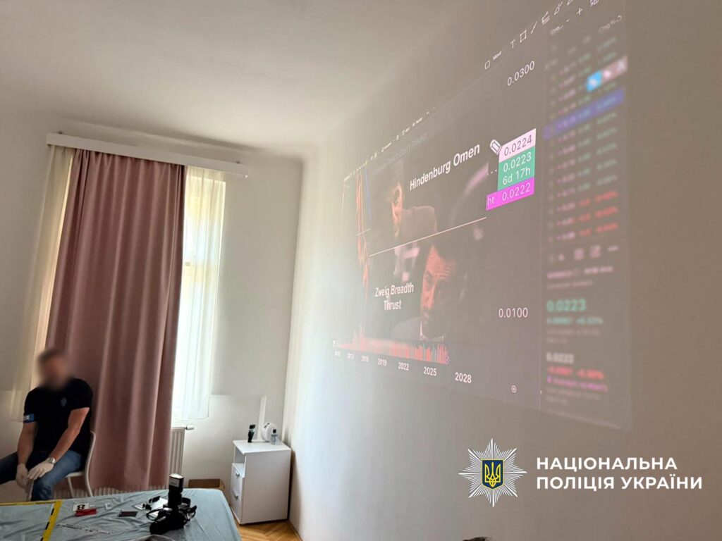 людина у формі правоохоронця біля сірої поверхні, на якій лежать речдоки, позаду нього вікно зі шторами, на стіні висвітлюється інформація, як при діафільмах