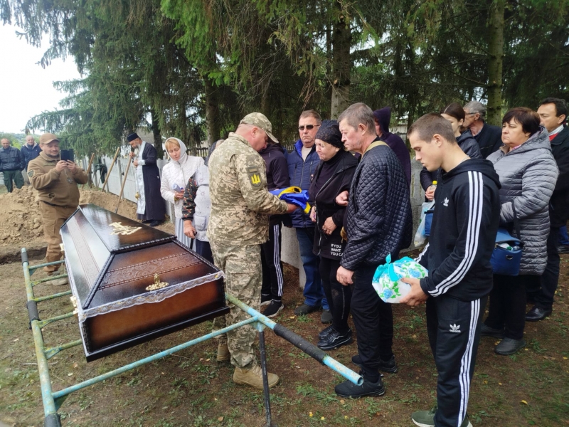 Воїн передає прапор з домовини полеглого бійця