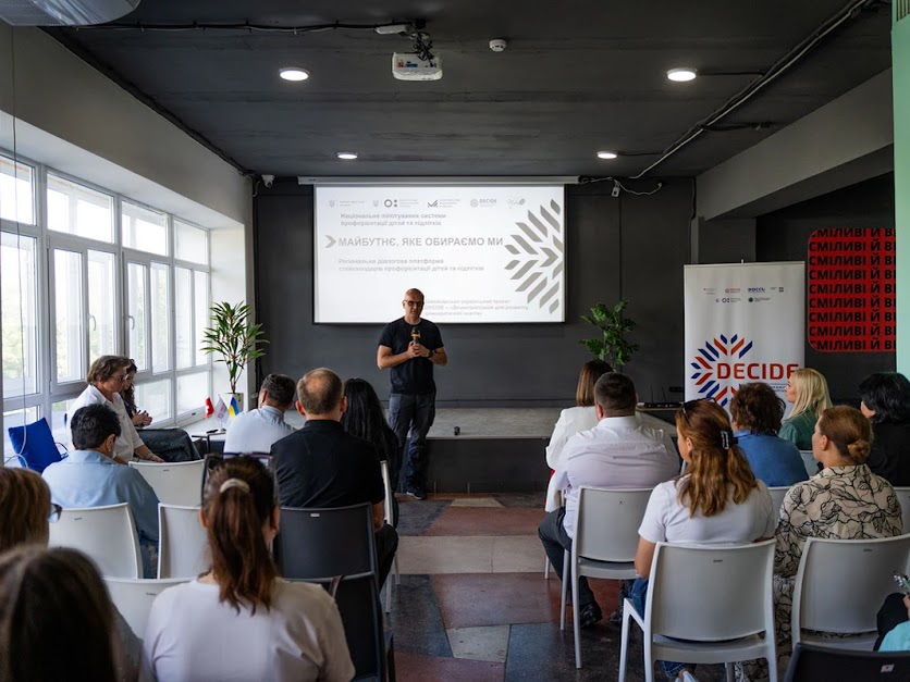 Євген Кончаковський на тлі екрану виступає перед аудиторією