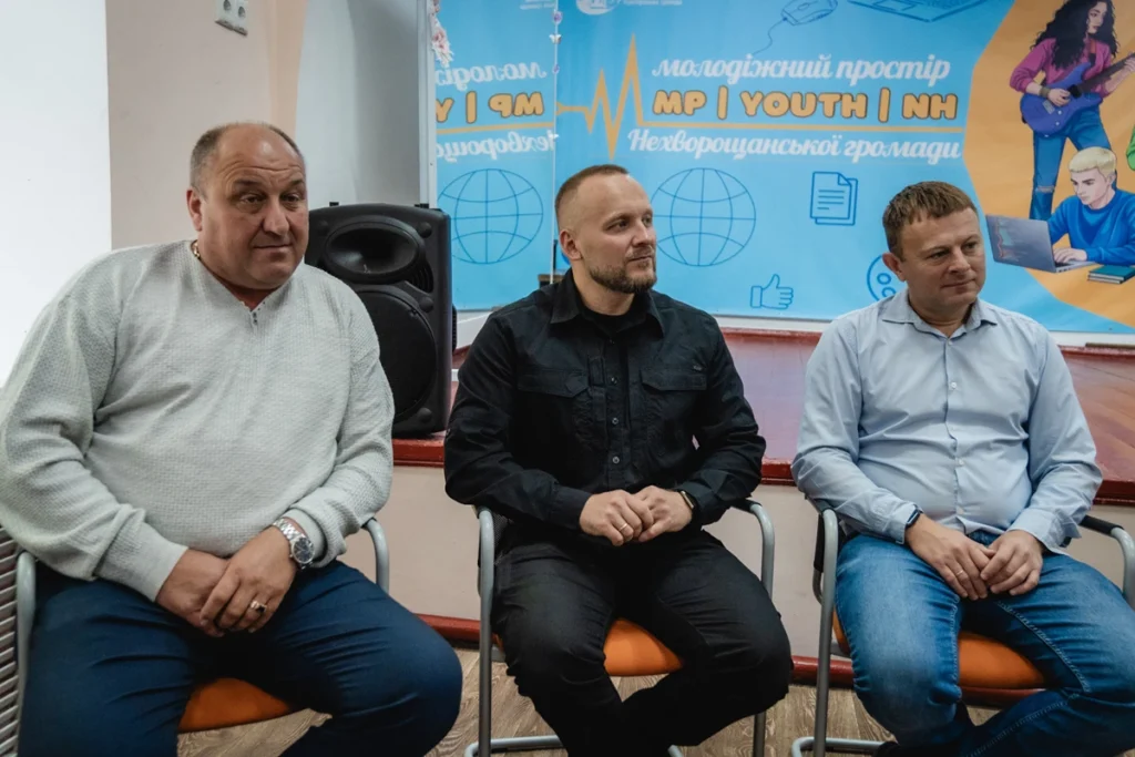 три людини сидять на стульцях.
