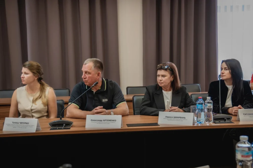 жінка, чоловік, дві жінки за столом, перед ними таблички з іменами, прізвищами, посадами