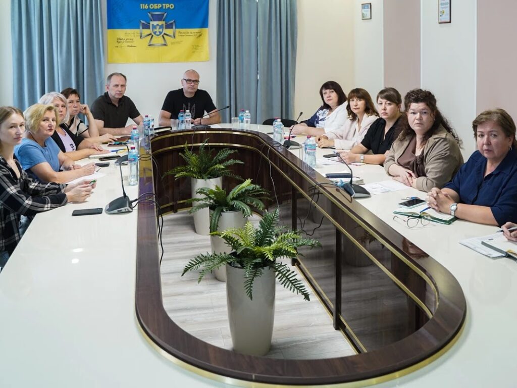 учасники наради за столом, на стіні - український прапор