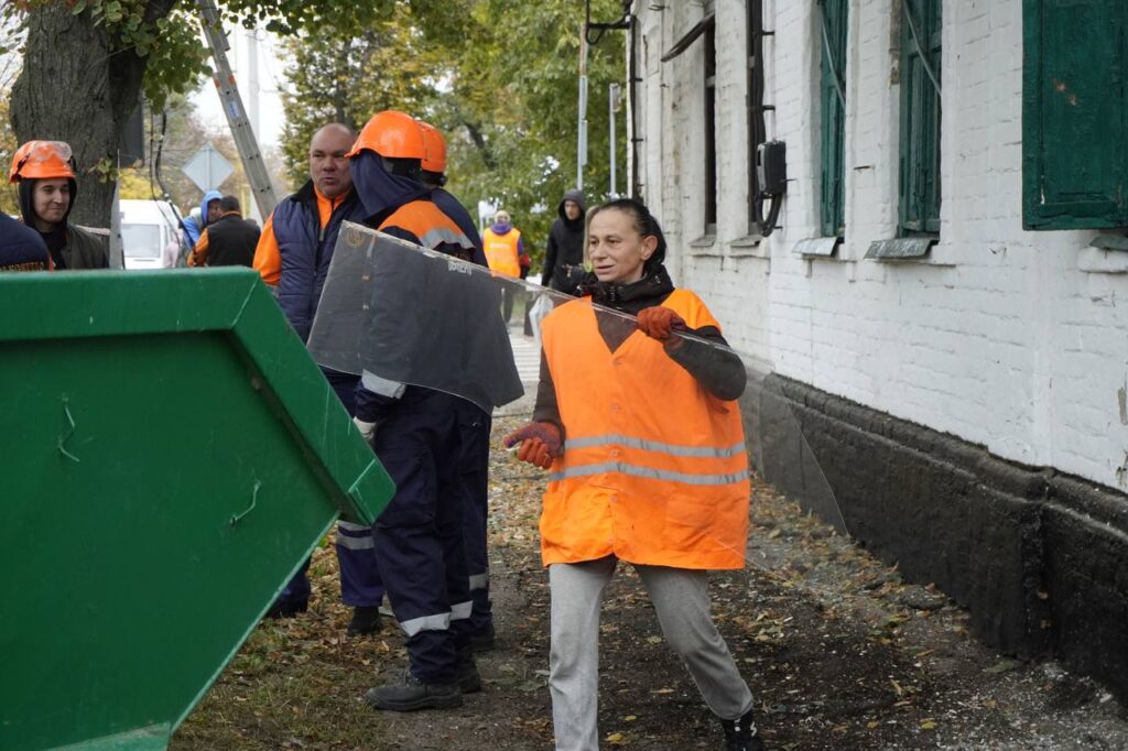 жінка з помаранчевому жилеті викидає уламок скла