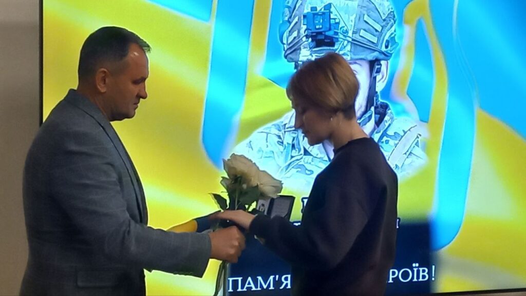 посадовець передає родичці полеглого воїна нагороду та квіти