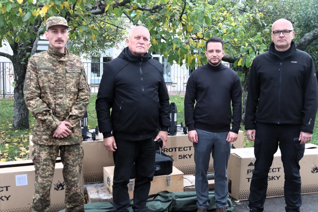 військовик та троє цивільних чоловіків біля коробок із дронами-перехоплювачами