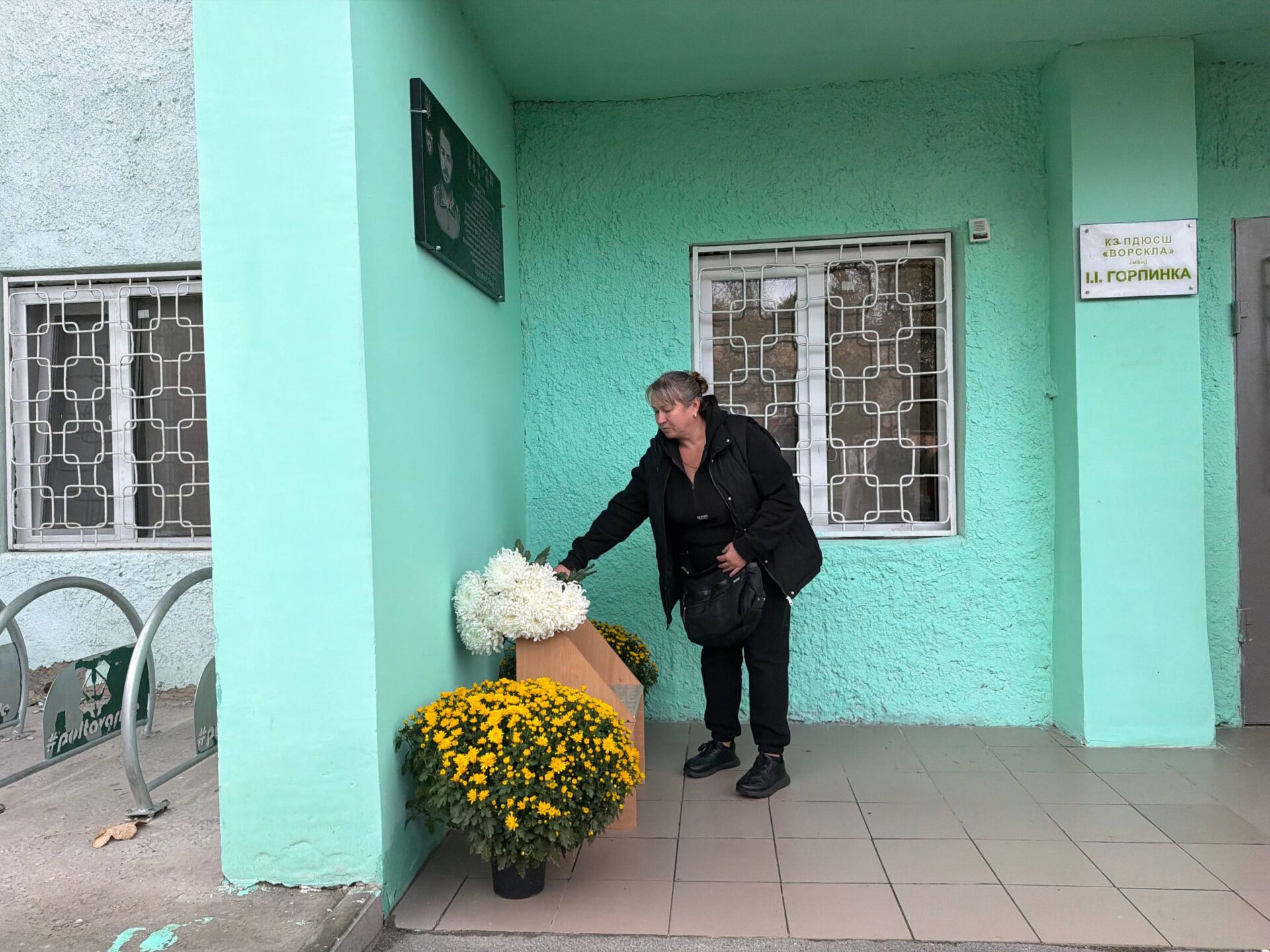 мати воїна кладе квіти до дошки