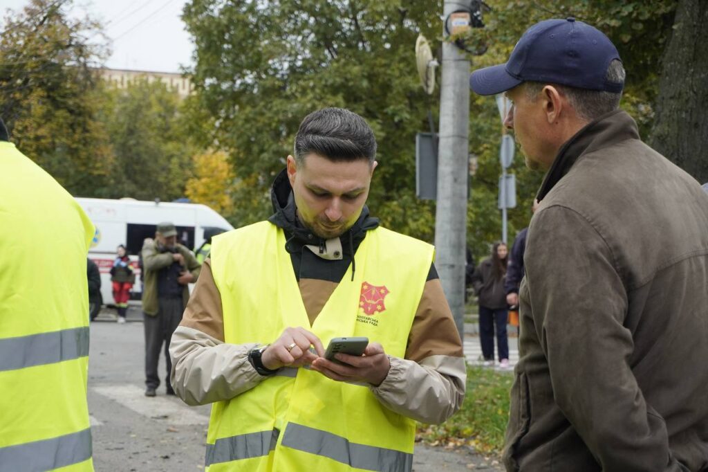 чоловік у жовтому жилеті записує інформацію чоловіка, який стоїть поруч, у телефон
