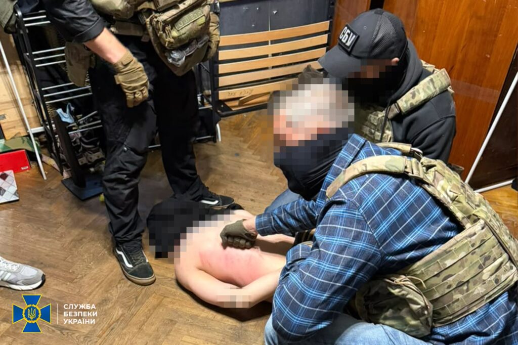 чоловік без верхньої частини одягу лежить із руками за спину та обличчям у підлогу, біля нього присіли двоє правоохоронців, а один стоїть 