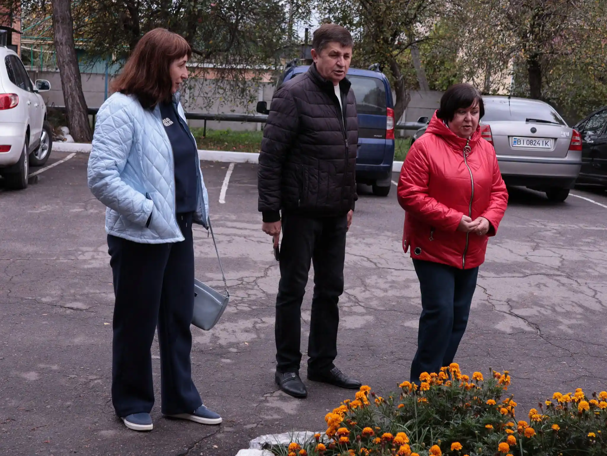 уповноважений і дві жінки стоять біля клумби поряд зі стоянкою авто
