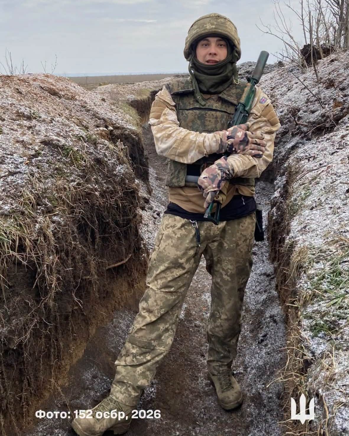 зима, військовик стоїть в окопі, тримаючи в руках зброю
