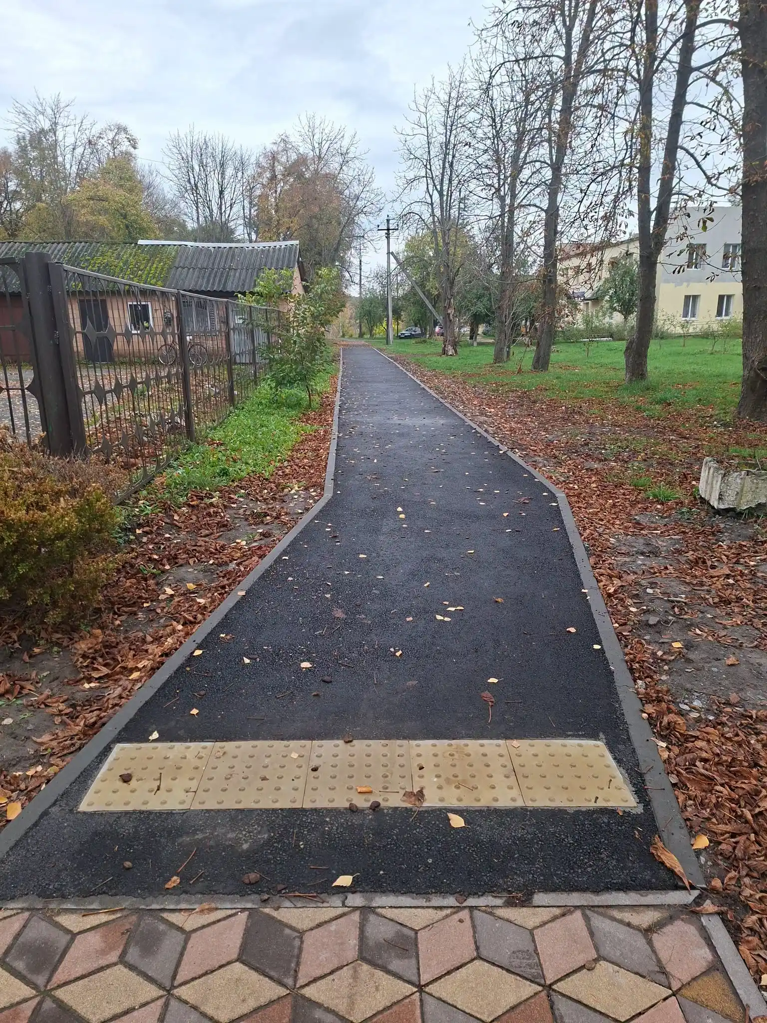 плиткова доріжка переходить у асфальтовану з позначкою для людей із порушенням зору