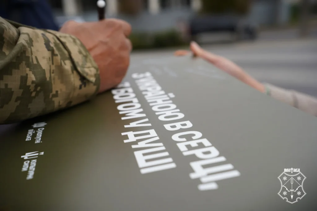 рука у військовій формі тримає маркер, яким підписують табличку "З Україною в серці, з богом у душі"