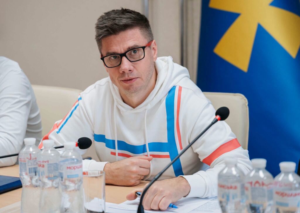 Олександр Біленький у білому світшоті за столом, позаду нього прапор Полтавщини