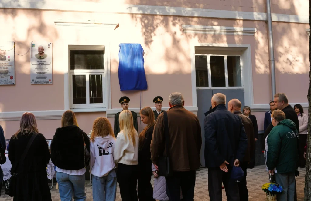 люди біля стіни, де встановлено меморіальну дошку