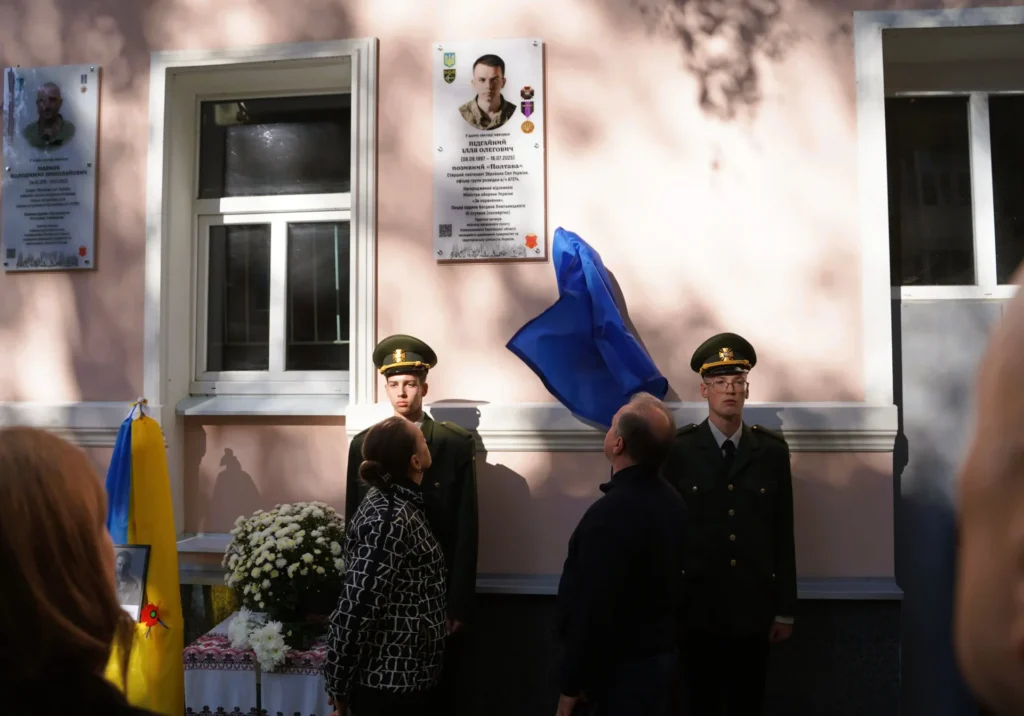 родичі знімають тканину з меморіальної дошки, поруч стоїть почесна варта