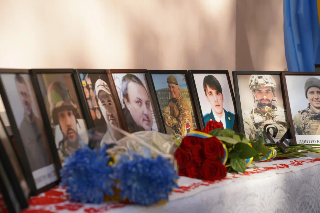 портрети полеглих захисників на столі, поруч із ними лежать квіти