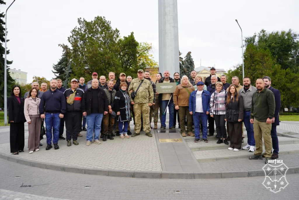 спільне фото біля державного прапора, один із чоловіків тримає в руках пам'ятну табличку