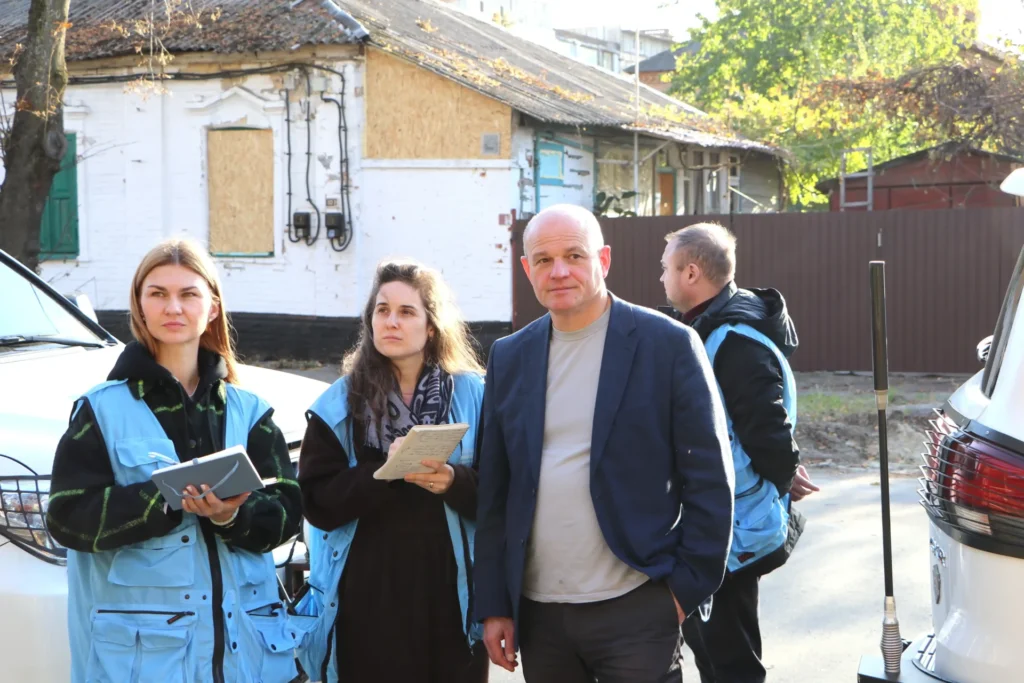 двоє жінок у жилетах ООН та Віталій Нікіпелов фіксують наслідки обстрілу