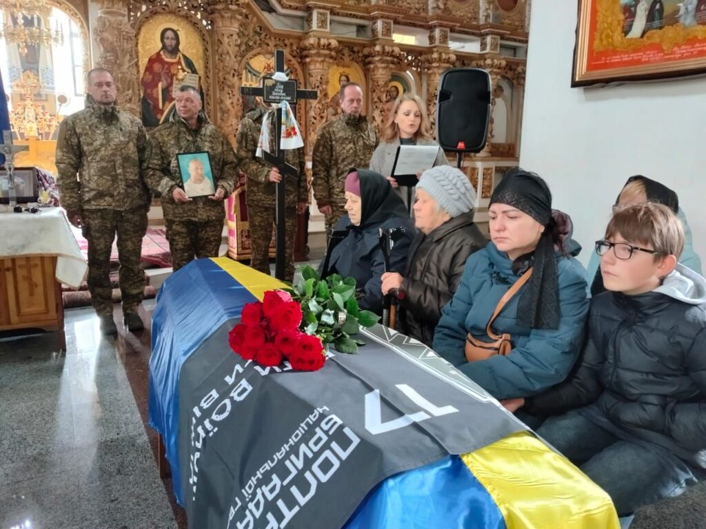 родичі полеглого сидять біля труни, накритої прапором