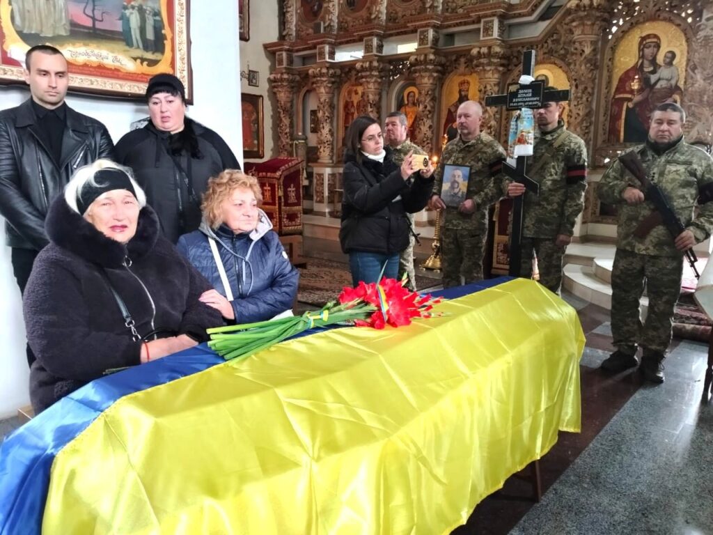 родичі полеглого сидять біля труни, накритої прапором